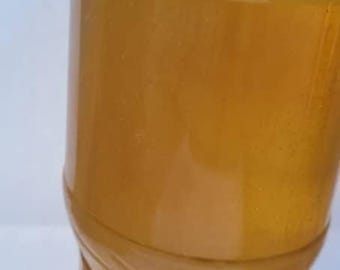 May include: A clear plastic bottle filled with a light brown liquid. The bottle has a rounded shape with a ridged base and a narrow neck. The liquid appears to be translucent.