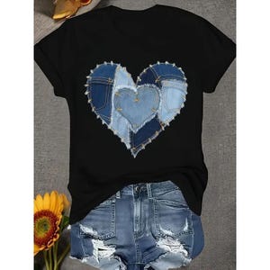 A black t-shirt with a heart-shaped design made of blue denim fabric, along with distressed denim shorts, placed on a gray surface.