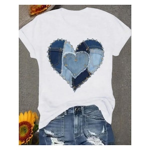 May include: White t-shirt featuring a heart design made from denim patches in various shades of blue. The heart is centered on the shirt, with a smaller heart shape in the middle. The shirt is paired with denim shorts.