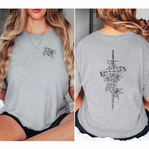 a woman wearing a grey shirt with a cross and flowers on it