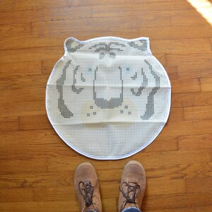 May include: White and grey embroidered tiger rug with a white background and grey tiger face. The rug is circular and has a textured surface.