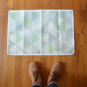 May include: A white and green geometric patterned rug with a white border. The rug is on a wooden floor.