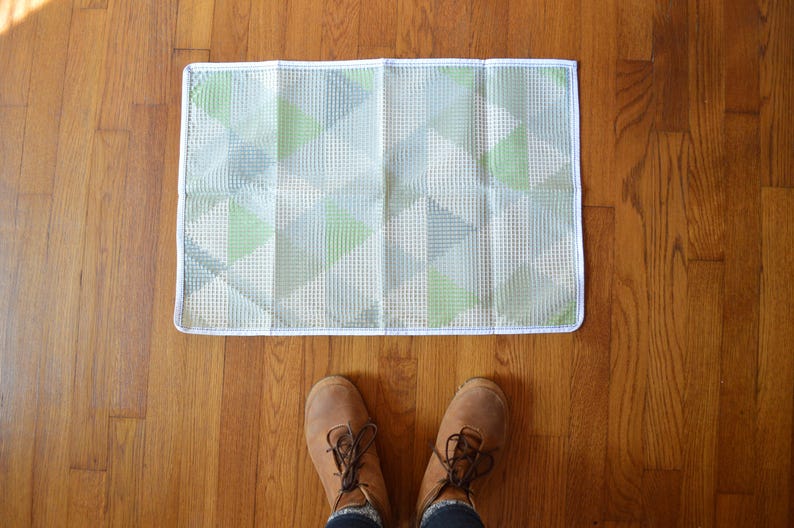 May include: A white and green geometric patterned rug with a white border. The rug is on a wooden floor.