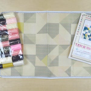 May include: A latch hook kit with a white canvas, colourful yarn, a hook, and instructions. The design features a geometric pattern of triangles and squares in shades of blue, pink, and yellow. The instructions include the text "Latch Hook Kit".