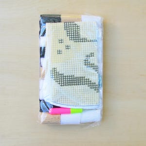 May include: A plastic-wrapped kit for creating a cross-stitch project. The kit includes a white canvas with a black and white design of a ghost, colourful threads, and a wooden needle.