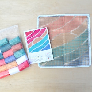 May include: A craft kit for creating a colorful tapestry with a rainbow design. The kit includes a canvas, yarn, a needle, and instructions.