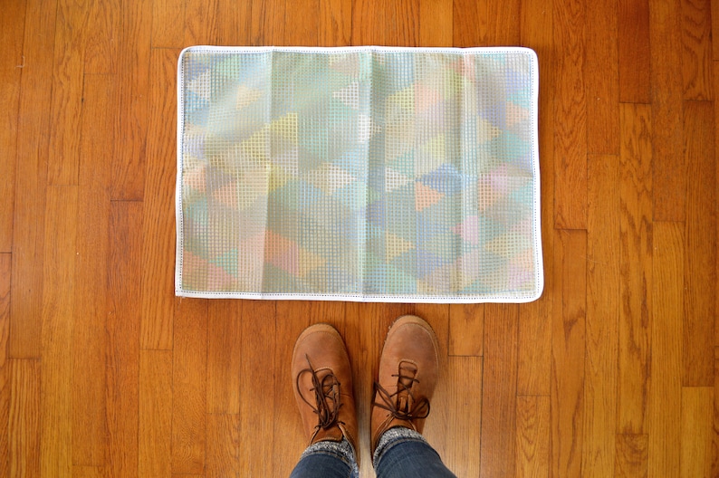 May include: A white doormat with an iridescent, grid-like pattern. The doormat is on a wooden floor.