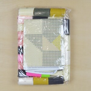 May include: A plastic-wrapped cross-stitch kit with a white canvas, colourful threads, and a geometric design. The design features a yellow, grey, and white pattern.
