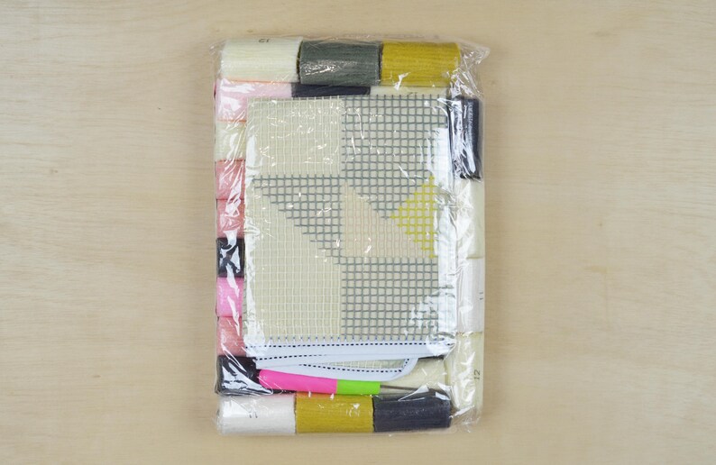 May include: A plastic-wrapped cross-stitch kit with a white canvas, colourful threads, and a geometric design. The design features a yellow, grey, and white pattern.