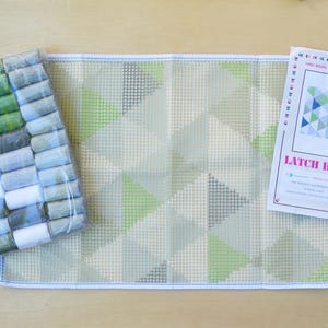May include: Latch hook kit with a green, blue, and gray geometric pattern. The kit includes a canvas, yarn, and a hook.