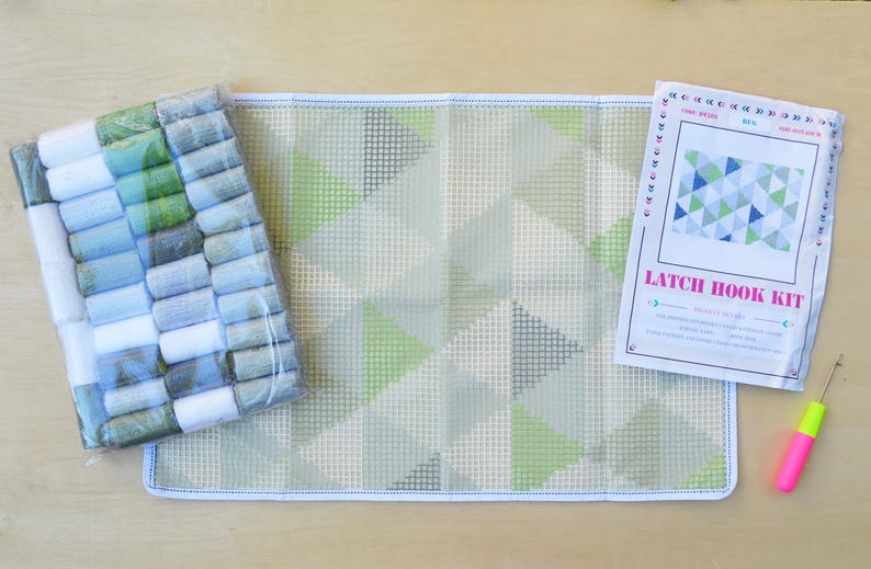 May include: Latch hook kit with a green, blue, and gray geometric pattern. The kit includes a canvas, yarn, and a hook.