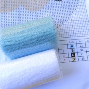 May include: Close-up of four skeins of embroidery floss, two white and two light blue. The floss is labelled with letters A, B, C, and D, and numbers 22, 37, 41, and 60. The floss is for cross-stitch embroidery.