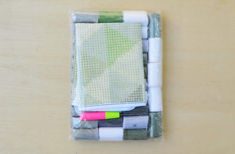 May include: A plastic-wrapped kit for cross-stitch embroidery. It includes a green and white canvas, floss in various colors, a needle, and instructions.