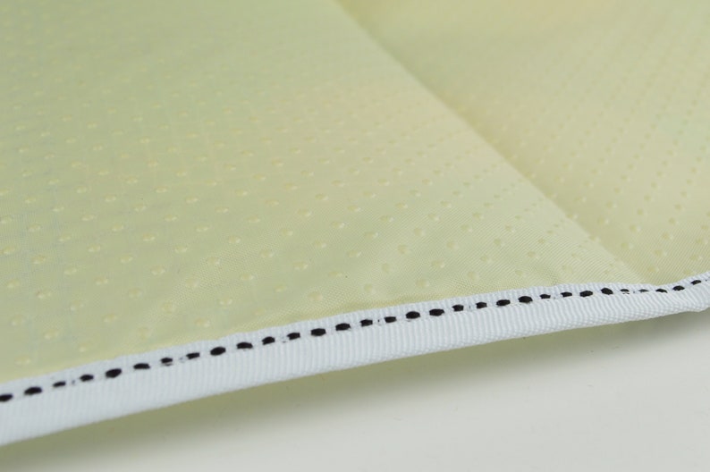 May include: Close-up of a light yellow fabric with a white trim and black stitching. The fabric has a subtle dotted pattern.