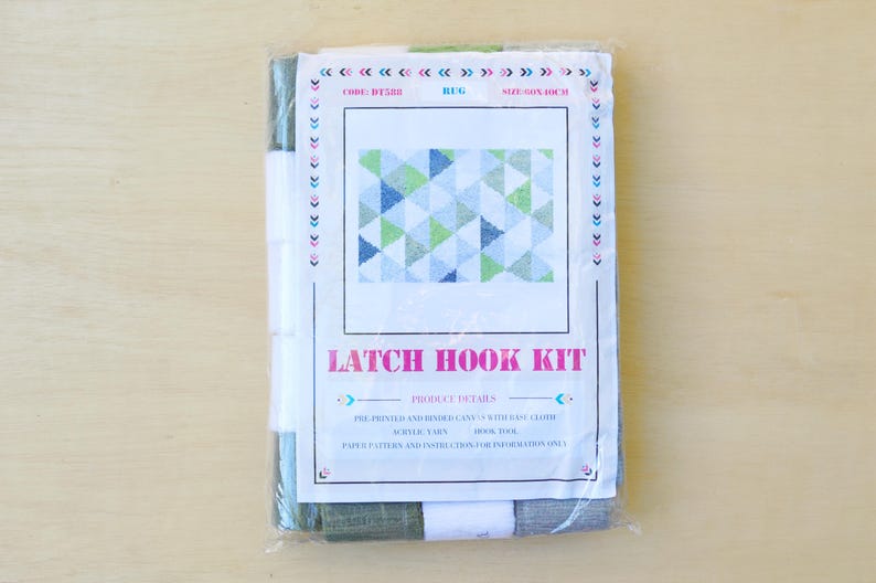 May include: A latch hook kit with a pre-printed canvas, yarn, and latch hook tool. The design features a geometric pattern of blue, green, and white triangles. The kit includes paper patterns and instructions for the project.