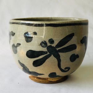 Puede incluir: Un pequeño cuenco de cerámica gris con un diseño de libélula negra. El cuenco tiene un fondo ligeramente redondeado y un borde ancho.