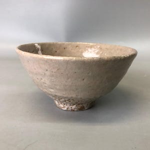 May include: A small, white ceramic bowl with a speckled glaze. The bowl has a rounded shape and a slightly flared rim.