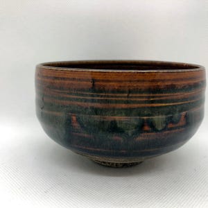 May include: A brown and green ceramic bowl with a striped pattern. The bowl is handmade and has a unique glaze.