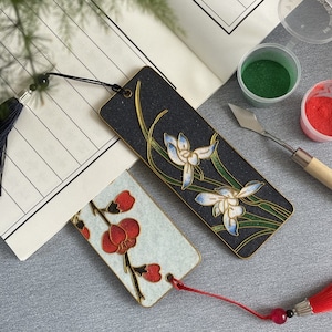 May include: Two decorative bookmarks with floral designs. One bookmark features a black background with white and blue flowers and green leaves. The other bookmark has a white background with red flowers and green leaves.