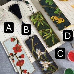 May include: Four different bookmark designs with various floral and nature themes. The bookmarks are made of wood and have a gold trim. The designs include a white background with red flowers, a black background with white flowers, a green background with bamboo, and a dark green background with yellow flowers.
