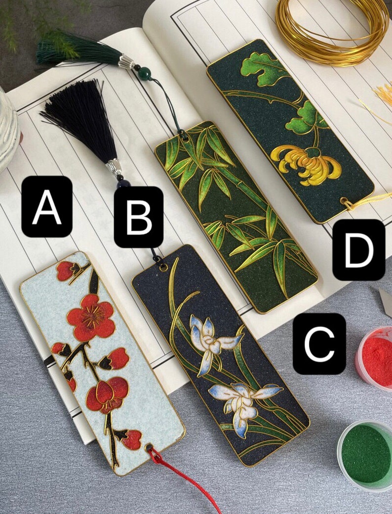 May include: Four different bookmark designs with various floral and nature themes. The bookmarks are made of wood and have a gold trim. The designs include a white background with red flowers, a black background with white flowers, a green background with bamboo, and a dark green background with yellow flowers.