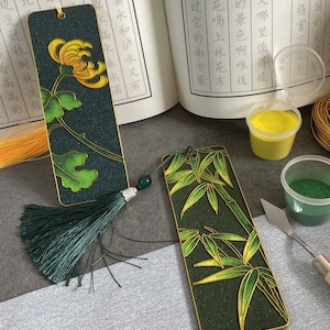May include: Two bookmarks with green and gold designs. One bookmark features a chrysanthemum flower and the other features bamboo. Both bookmarks have a green tassel.