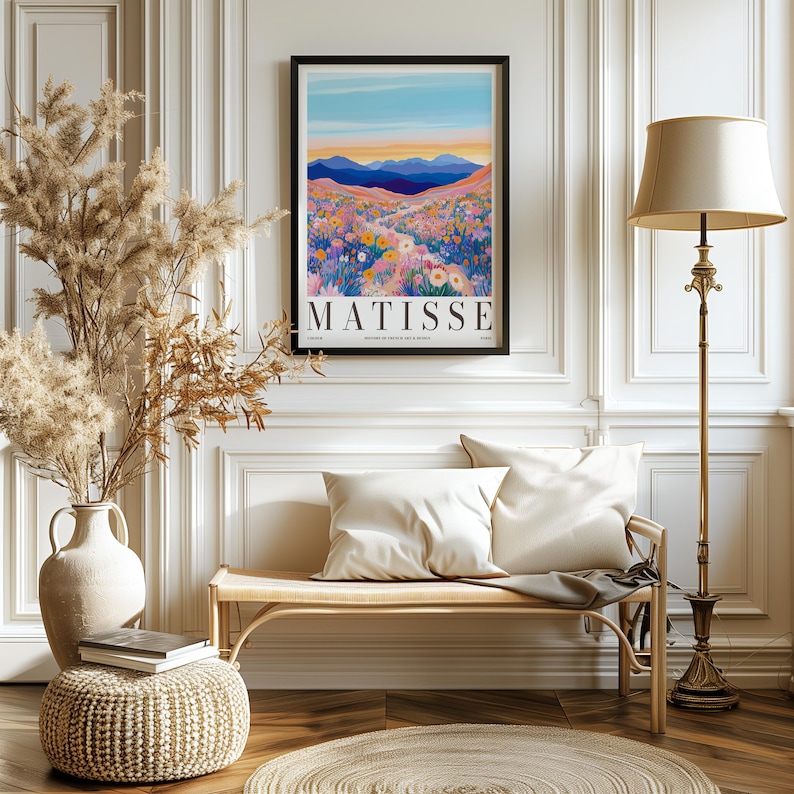 May include: A framed poster with a colorful illustration of a mountain landscape with a path leading through a field of flowers. The poster is titled "MATISSE" and is hanging on a white wall in a room with a wooden bench and a floor lamp.