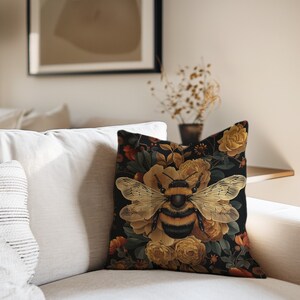 Puede incluir: Una almohada negra con un patr&oacute;n floral que presenta un gran abejorro en el centro. Las flores son amarillas y naranjas con hojas verdes. El fondo es negro.