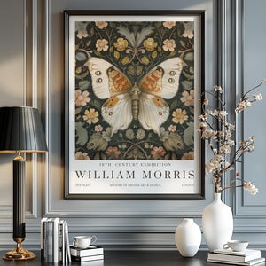 May include: A framed art print of a butterfly with cream and orange wings, set against a dark floral background. The print is labelled "19th Century Exhibition William Morris". The artwork is displayed on a wall, with a lamp and vases.