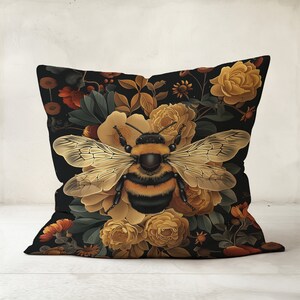 Puede incluir: Una almohada negra con un patr&oacute;n floral que presenta un gran abejorro en el centro. Las flores son amarillas, naranjas y marrones.