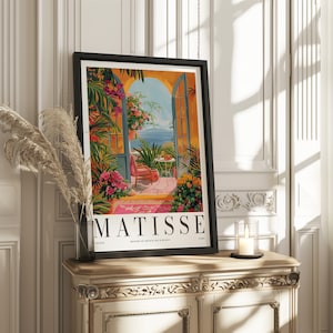 May include: A framed poster with a colorful painting of a patio scene with a view of the ocean. The poster has the text "MATISSE" in large black letters at the bottom. The poster is titled "Masters of French Art & Design".