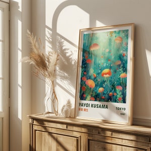 K&ouml;nnte beinhalten: Ein gerahmtes Poster mit einer farbenfrohen Illustration von Quallen in einem t&uuml;rkisfarbenen und gr&uuml;nen Ozean. Das Poster tr&auml;gt den Titel "Yayoi Kusama" mit dem Text "Tokyo 1987" in der rechten unteren Ecke.