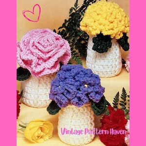 May include: Crocheted flower arrangements in pink, yellow, and blue, with green leaves and white bases. The text "Vintage Pattern Haven" is visible. The flowers are arranged on a yellow surface with a pink border and a heart graphic.