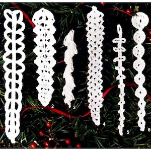 Puede incluir: Seis adornos navideños blancos hechos a mano con ganchillo. Los adornos presentan varios diseños, incluyendo patrones calados y estilos con cuentas. Se muestran sobre un fondo de agujas de pino verdes, bayas rojas y una cinta roja.