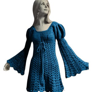 Puede incluir: Un vestido de crochet azul con mangas acampanadas y escote cuadrado. El vestido tiene un lazo en la cintura y un dobladillo festoneado.