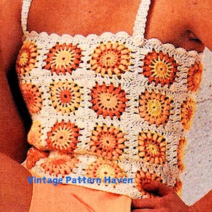 May include: A crochet top with a white background and orange, yellow, and peach colored flowers. The top has a scalloped edge and thin straps.