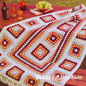 May include: A vintage crochet blanket with a granny square design. The blanket features a white background with colorful squares in red, yellow, blue, and orange. The blanket has a fringed edge and the text "Vintage Pattern Haven" is visible.