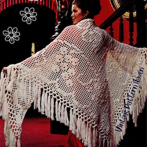 Puede incluir: Chal de ganchillo color crema con un patrón geométrico y largas borlas. El chal está drapeado sobre los hombros, mostrando su diseño de tejido abierto. El texto "Vintage Pattern Haven" es visible en el chal.