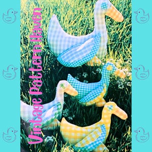 Peut inclure: Cinq peluches de canard en tissu faits à la main dans une variété de motifs vichy bleus et jaunes. Les canards sont disposés en rangée sur un lit d'herbe verte. Les canards sont tous tournés vers le côté droit de l'image. L'image est intitulée "Vintage Pattern Haven".