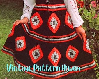 Peut inclure: Une jupe en crochet avec un fond noir et des motifs en forme de losange rouge, gris et blanc. La jupe a une large bordure rouge, grise et blanche autour du bas.