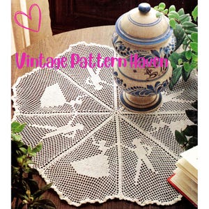 Peut inclure: Un napperon en crochet blanc avec un motif floral délicat. Le napperon est circulaire et a un bord festonné. Il est placé sur une table en bois avec un pot en céramique au centre.