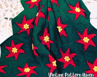May include: A green crocheted blanket featuring a repeating pattern of red star-shaped flowers with yellow centers. The blanket has a textured appearance and is folded, displaying the design. The text "Vintage Pattern Haven" is visible in the lower right corner.
