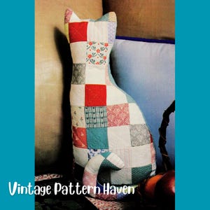 Peut inclure: Un coussin en forme de chat rembourré, fabriqué à partir d'un assemblage de carrés de tissus variés. Le textile présente une grille de couleurs incluant le rouge, le bleu sarcelle, le blanc et le rose pâle, avec des motifs floraux et rayés.