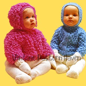 May include: Two babies wearing knitted hats and sweaters. The baby on the left is wearing a pink sweater with a matching hat, while the baby on the right is wearing a blue sweater with a matching hat. Both babies are wearing white knitted pants.