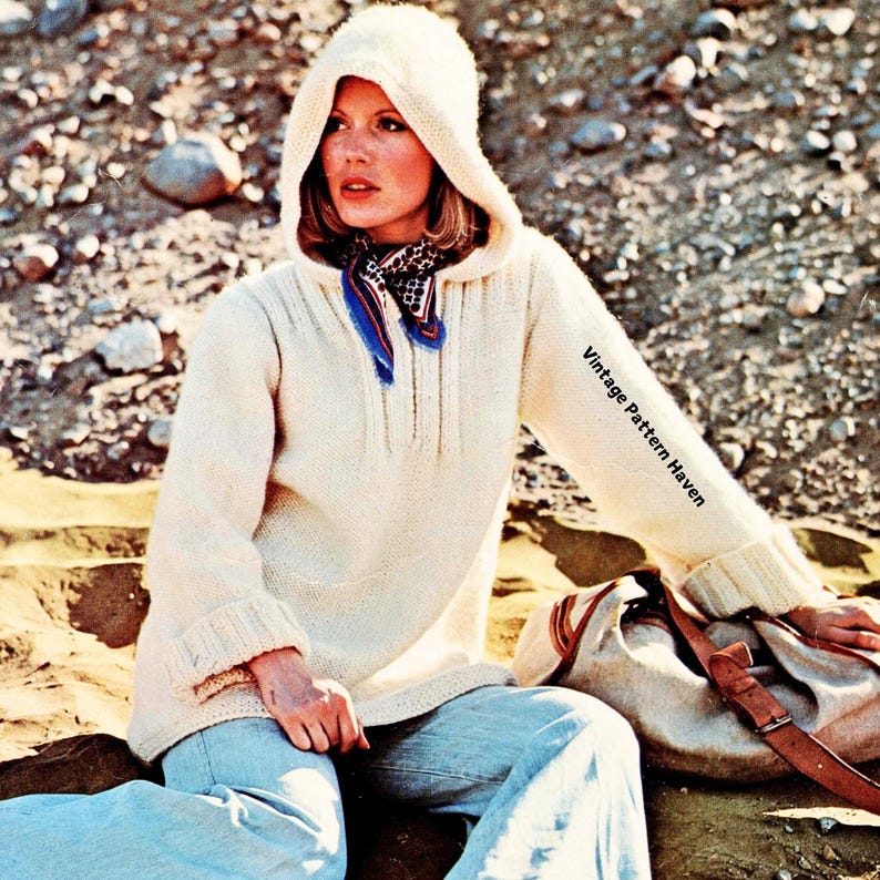 Puede incluir: Un su&eacute;ter blanco de punto con capucha y una bufanda de estampado azul y blanco. El su&eacute;ter tiene una textura acanalada y un corte largo y holgado. La modelo lleva pantalones vaqueros azules y un bolso de cuero marr&oacute;n.