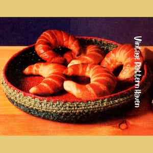 May include: A woven basket with a red interior holds several golden-brown croissants. The basket has a green and black woven rim. The text "Vintage Pattern Haven" is printed vertically on the right side of the image.