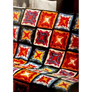 Peut inclure: Une couverture en crochet colorée avec un motif géométrique de carrés dans des tons de rouge, orange, jaune, vert, bleu et blanc.