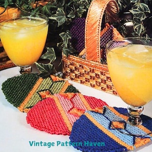 May include: Four colorful crocheted coasters with a geometric design. The coasters are made with a variety of colors, including green, pink, blue, and yellow. The coasters are sitting on a white surface with two glasses of orange juice.