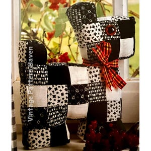 May include: Black and white patchwork fabric dog toy with a red and yellow ribbon around its neck. The dog toy has a button eye.