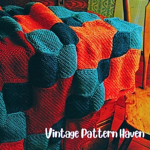 May include: A colorful, knitted blanket with a patchwork design. The blanket features squares in shades of teal, navy, and orange. The text "Vintage Pattern Haven" is visible at the bottom. The blanket is draped over a wooden surface.